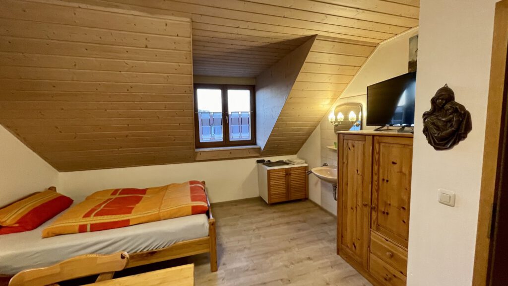 Einzelzimmer mit Dachschräge, Bett und Fernseher